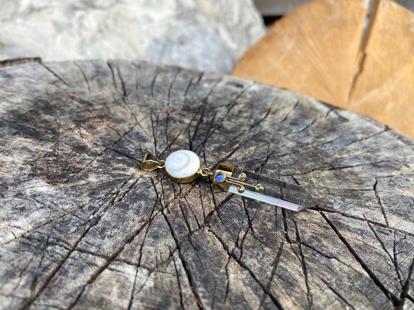Pendant rock crystal with operculum with spirals, dots and small stone, brass