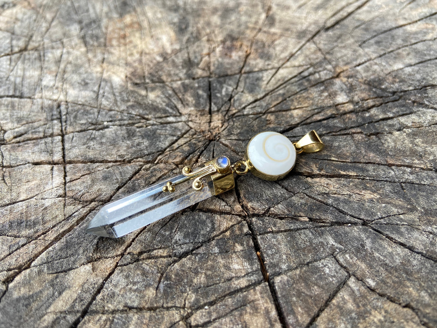 Pendant rock crystal with operculum with spirals, dots and small stone, brass