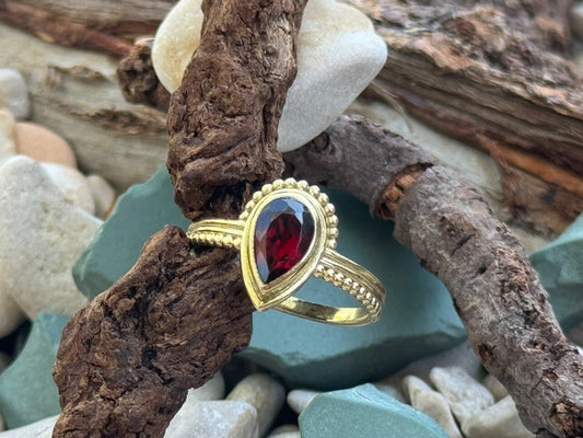Ring mit facettiertem rotem Granat in Tropfenform aus Messing